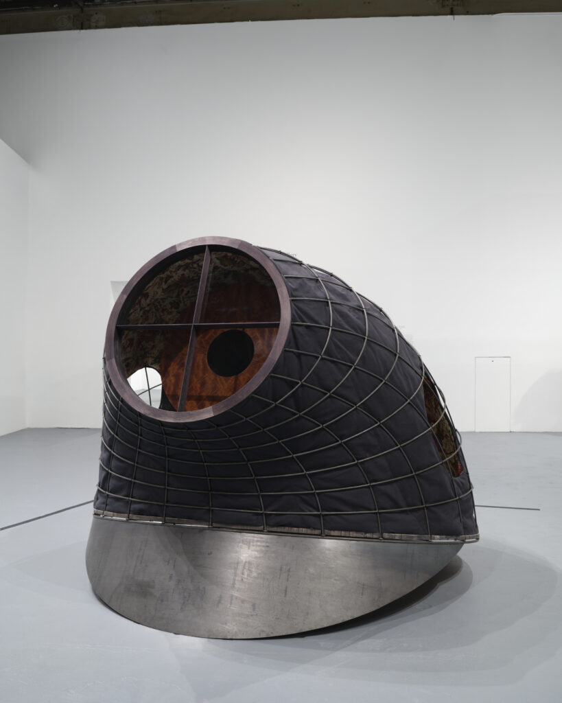 Sculpture in the shape of civil war cap with latticed exterior, steel brim, and crosshair at the top