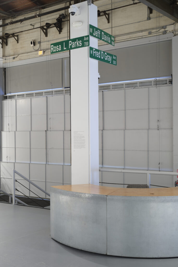 Three green street signs installed on a column. One sign reading "Rosa L. Parks Ave" hangs from one side side. Two signs reading "W Jeff Davis Ave" and "W Fred D Gray Ave" hangs from another side
